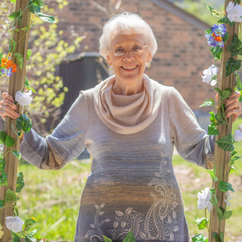 An elderly lady holding up a frame and smiling.