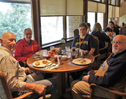 VMP West Allis Senior Community Club members enjoy a tailgate luncheon, four seniors sitting around the table in brewers gear