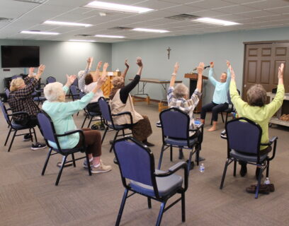 VMP West Allis Senior Community Club ladies in an exercise class, sitting with hands raised